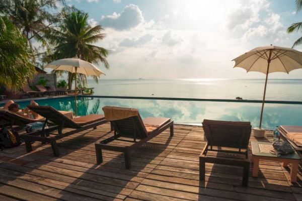 A serene poolside view with lounge chairs, umbrellas, and a calm sea beneath a partly cloudy sky, creating an idyllic tropical scene.