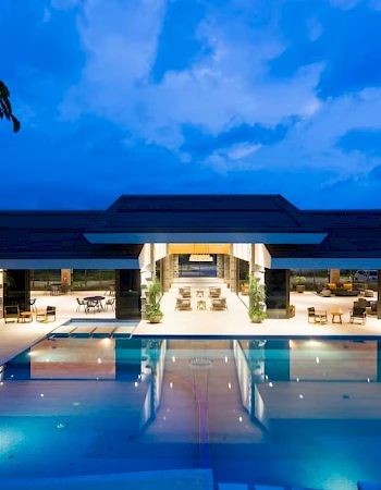 A luxurious resort pool area with modern architecture, surrounded by lounge chairs and illuminated by soft ambient lighting in the evening.
