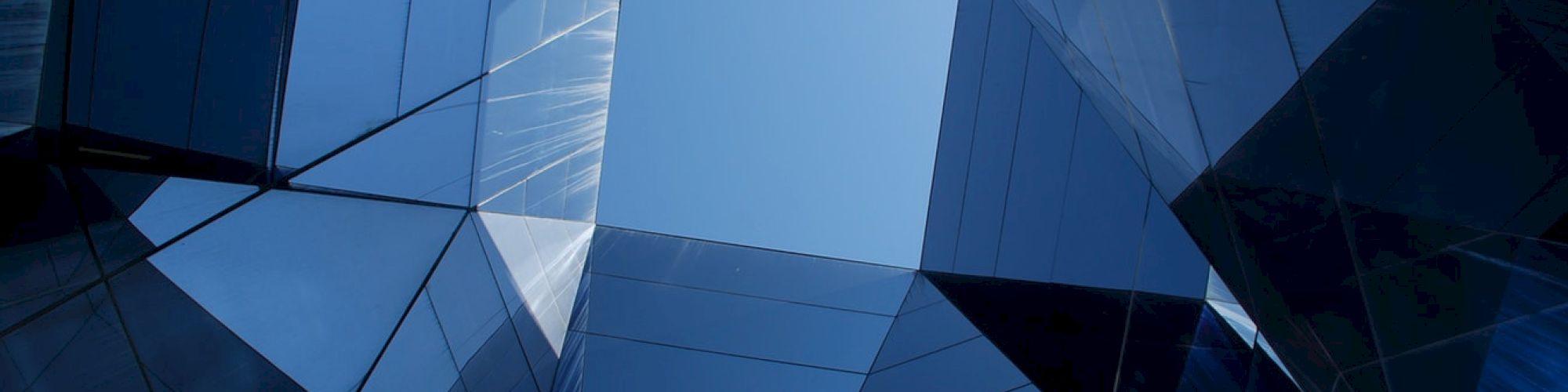 The image shows an upward view of a modern, glass-covered architectural structure with an open sky visible through a geometric gap.