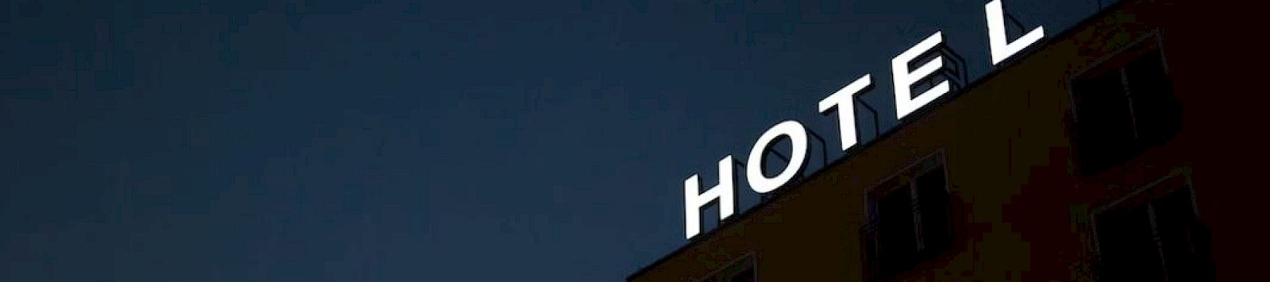 The image shows a dimly lit building at night with a bright neon sign reading "HOTEL" on top.
