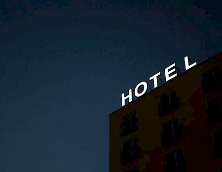 The image shows a dimly lit building at night with a bright neon sign reading "HOTEL" on top.