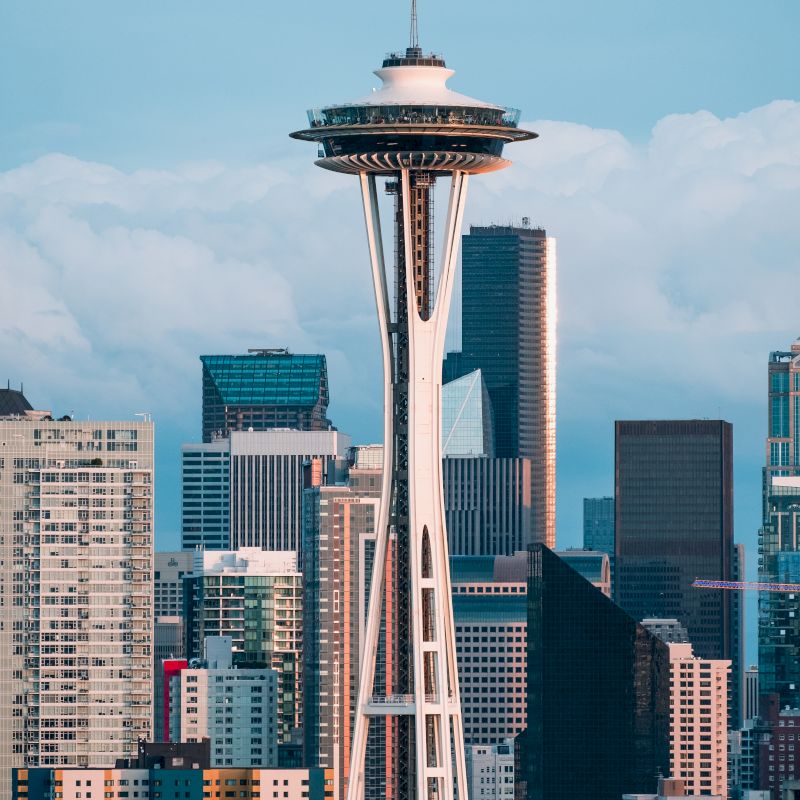 The image displays a cityscape with a prominent observation tower, surrounded by modern buildings under a partly cloudy sky.