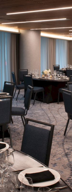 The image shows an elegantly set dining room with round tables, black chairs, and tableware, ready for a formal event or banquet.