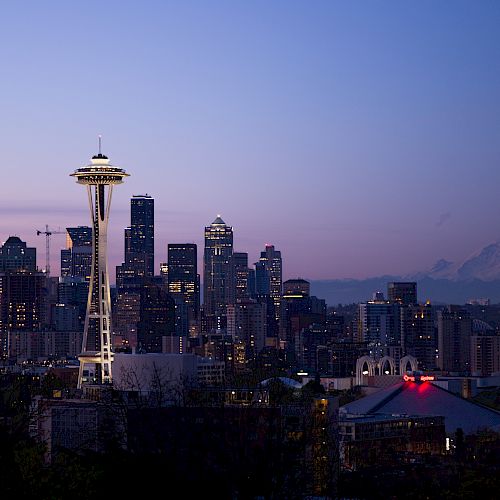 This image shows the Seattle skyline at dusk, featuring the Space Needle and Mount Rainier in the background against a twilight sky.