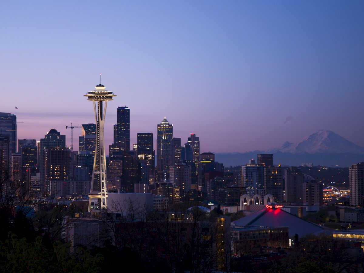 This image shows the Seattle skyline at dusk, featuring the Space Needle and Mount Rainier in the background with a clear sky.