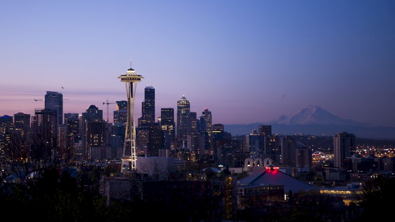 This image shows the Seattle skyline at dusk, featuring the Space Needle and Mount Rainier in the background with a clear sky.
